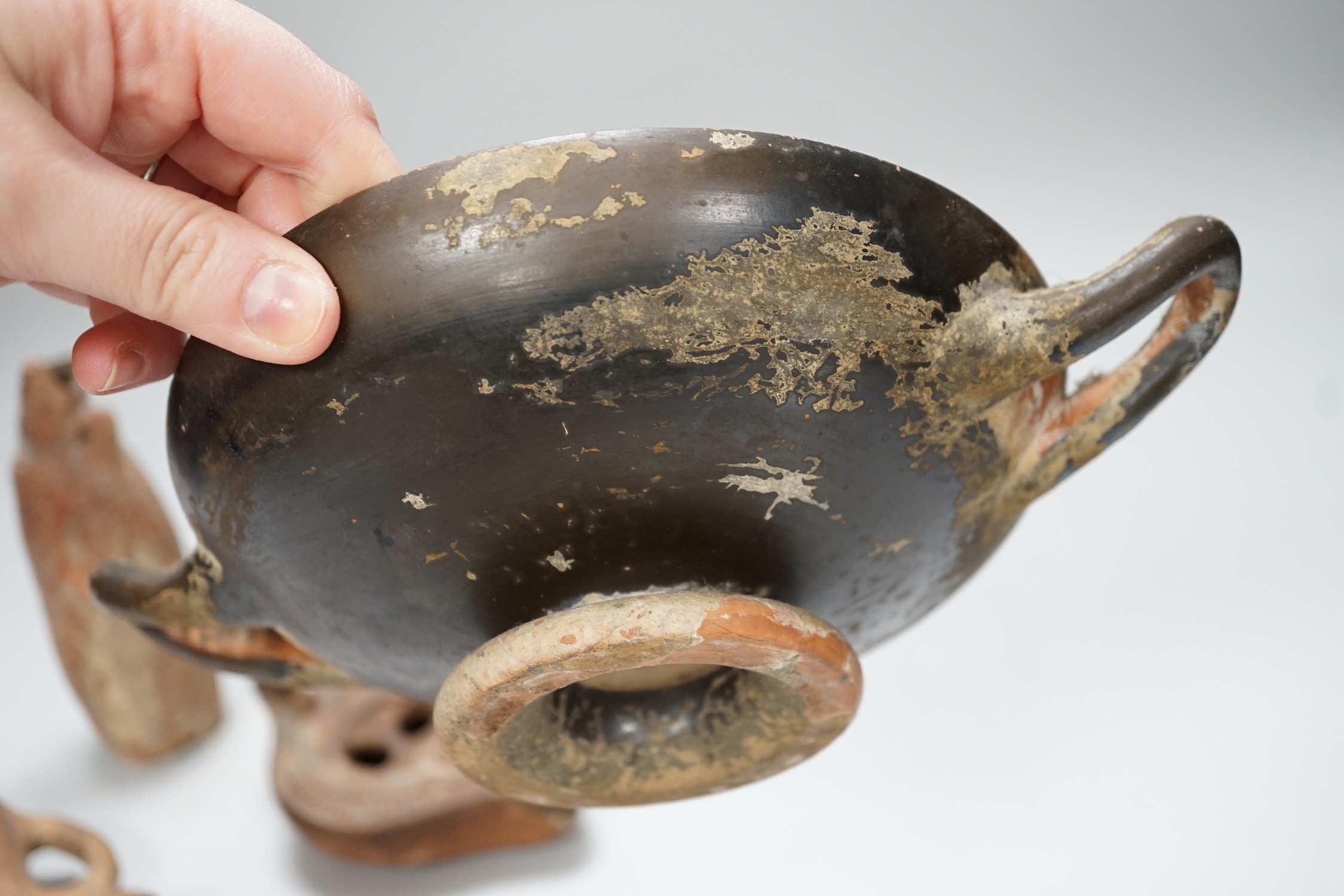 An Apulian black painted kylix, c. 4th century BCE., a Cypriot pottery flask, early Iron Age, two Roman terracotta oil lamps and another archaic vessel, tallest 14cm